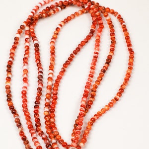 May include: A strand of red and white carnelian beads. The beads are round and have a smooth, polished finish.