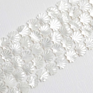 Pode incluir: Arranjo diagonal de pequenos elementos decorativos brancos em forma de concha sobre um fundo branco texturizado. As conchas têm um brilho perolado, que reflete a luz. O design cria uma estética delicada e elegante. Provavelmente feitas de cerâmica.