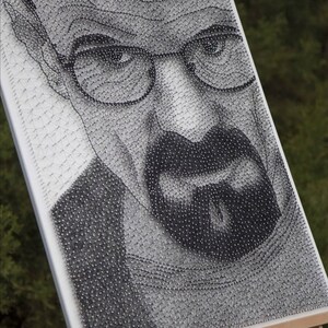May include: A black and white portrait of a man with a mustache and glasses, created using a grid of nails and string.