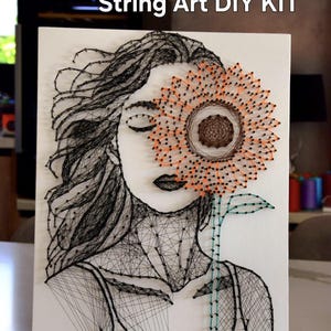 May include: String art DIY kit featuring a woman's face with a sunflower covering one eye. The artwork is created with black string on a white pre-nailed board. The sunflower is orange and brown. Text on the image reads "String Art DIY KIT" and "Pre-nailed board kit".