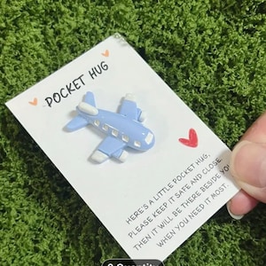 Könnte beinhalten: Eine weiße Karte mit einem blauen und weißen Flugzeug-Anhänger. Die Karte trägt den Text "Pocket Hug" und "Here's a little pocket hug, please keep it safe and close. Then it will be there beside you when you need it most."