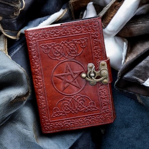 Könnte beinhalten: Ein braunes Lederjournal mit einem Pentagramm-Design und einem Metallverschluss. Das Journal ist geschlossen und liegt auf einer blauen Jeans-Oberfläche.