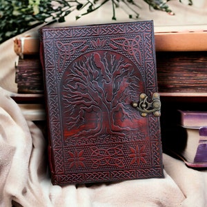 Può includere: Un diario in pelle marrone con un design ad albero della vita in rilievo sulla copertina. Il diario ha una chiusura in ottone ed è chiuso.