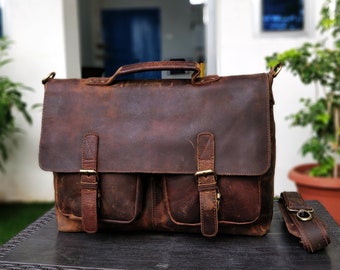 May include: A brown leather briefcase with two front pockets and a long strap. The bag has a distressed look and is made of high-quality leather.
