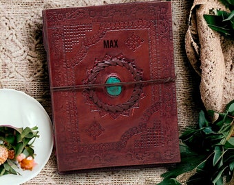 May include: A brown leather journal with intricate embossed designs and a turquoise stone embellishment. The journal has a closure strap and the name "MAX" is embossed on the front cover.