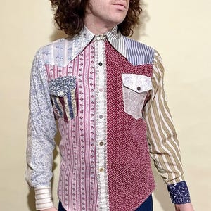 Puede incluir: Una camisa patchwork con una variedad de patrones y colores. La camisa presenta diseños florales, a rayas y de cachemira en tonos de azul, rojo y crema. Tiene cuello y puños abotonados.