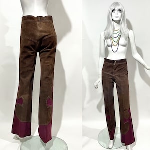 Könnte beinhalten: Braune Wildlederhose mit ausgestelltem Bein-Design und burgunderfarbenen Akzenten. Die Hose wird auf einer Schaufensterpuppe präsentiert, die den Vintage-Stil und die einzigartige Farbkombination zeigt. Die Hose hat eine hohe Taille und eine taillierte Passform.