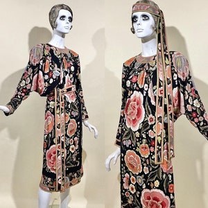 May include: Two mannequins wearing long black dresses with floral patterns. The dresses have a gold trim and the mannequins are wearing headbands.