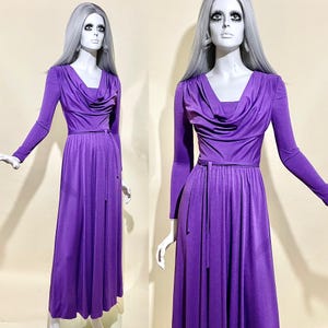 May include: A long-sleeved, purple maxi dress with a cowl neck and a tie belt. The dress is made of a soft, flowing fabric.
