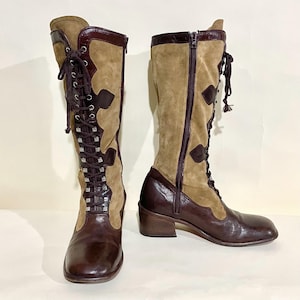 Peut inclure: Bottes hautes marron et beige. Ces bottes combinent cuir et daim, avec un laçage sur le devant et une fermeture éclair latérale. Le design comprend des découpes décoratives et un petit talon.