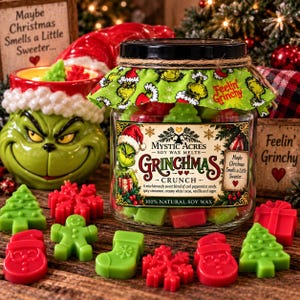 Puede incluir: Un frasco de vidrio lleno de ceras aromáticas rojas y verdes con formas de árboles de Navidad, hombres de jengibre, calcetines y copos de nieve. El frasco tiene una etiqueta que dice Mystic Acres Grinchmas Crunch y una tapa de tela verde.