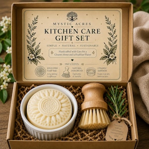 Può includere: Una scatola regalo in cartone marrone contenente un set per la cura della cucina. All'interno si trovano una pirofila in ceramica bianca con un sapone solido a forma di girasole, una spazzola per piatti in legno e un rametto di rosmarino.