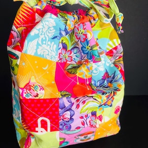 May include: A colorful drawstring bag with a patchwork design. The bag features a variety of vibrant floral and geometric patterns in shades of pink, blue, yellow, and green. The drawstring is a light green with a floral pattern.