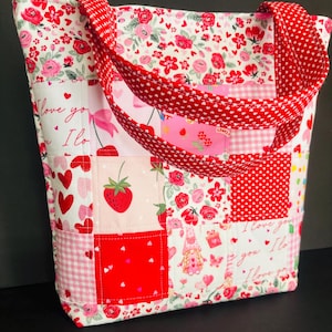 May include: A patchwork tote bag with a variety of patterns, including red hearts, strawberries, and floral designs. The bag features red handles with white polka dots and the text "I love you".