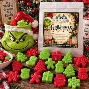 May include: A green ceramic mug shaped like a character face wearing a Santa hat, accompanied by a white bag labeled Mystic Acres Grinchmas Soy Wax Melts, and various red and green holiday-themed wax shapes including trees, gifts, and snowmen.
