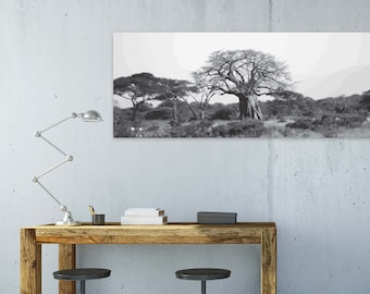 Op de afbeelding: Een zwart-wit landschapsfoto van bomen hangt boven een houten bureau. Een zilveren bureaulamp, boeken en twee zwarte krukken maken de kantoorinrichting compleet. Het bureau is gemaakt van natuurlijk hout.