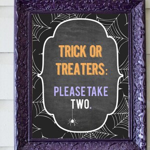 May include: A black chalkboard sign with a white frame and a spiderweb design. The sign says "Trick or Treaters: Please Take Two."