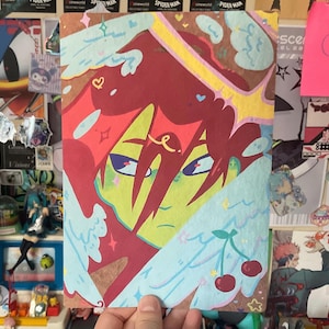 Könnte beinhalten: Eine farbenfrohe Illustration mit einem stilisierten Gesicht mit roten Haaren, grüner Haut und blauen Augen. Das Kunstwerk enthält Engelsflügel, Kirschen und dekorative Elemente. Der Hintergrund ist eine Collage aus verschiedenen Aufklebern und Postern.