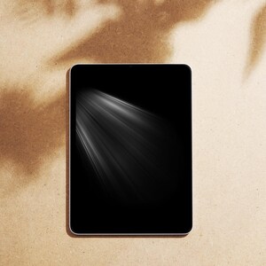 May include: A black tablet with a white border, showing a bright, white light effect radiating from the upper left. The tablet is on a textured, tan background with shadow patterns.