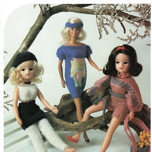 May include: A Studley knitting pattern 428 for a five-in-one outfit to fit 11/12 inch dolls. The image shows three dolls wearing hand-knitted garments: a white and black two-piece set, a blue dress with a headband, and a pink romper with a matching bag.