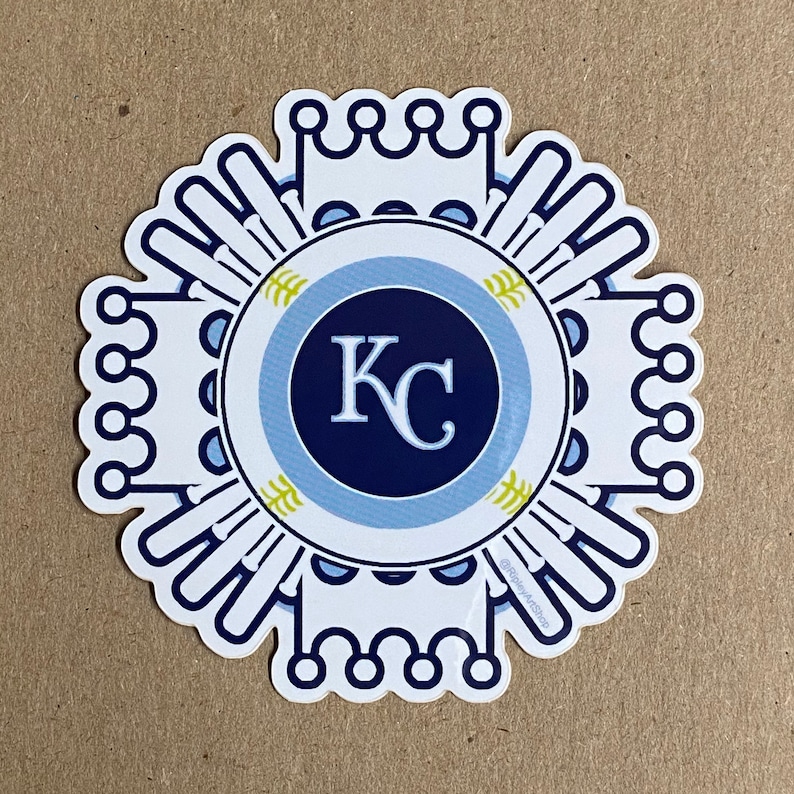 Pode incluir: Etiqueta branca com um design circular azul e azul claro. O centro do c&iacute;rculo tem um c&iacute;rculo azul marinho com as letras "KC" em branco. A etiqueta tem um design de coroa ao redor da borda externa.