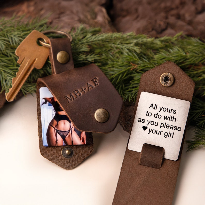 May include: A brown leather keychain with a photo inside and a key attached. The keychain has the initials "MB+AE" embossed on the front. The open flap reveals a card with the text "All yours to do with as you please your girl."