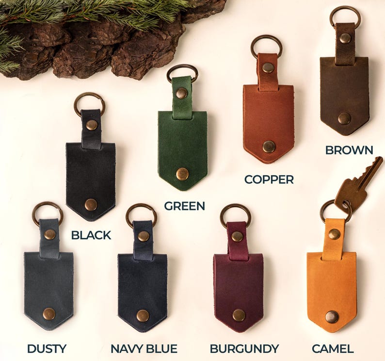 May include: A collection of leather keychains in various colors, including black, green, copper, brown, dusty, navy blue, burgundy, and camel. Each keychain features a metal ring and a snap closure. The word "BROWN" is printed on one of the keychains.