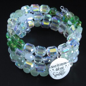 May include: A multi-strand wrap bracelet featuring clear iridescent faceted beads and vibrant green beads. A round silver-toned metal charm is attached, engraved with the text "Never let anyone dull your Sparkle" accompanied by small star icons.
