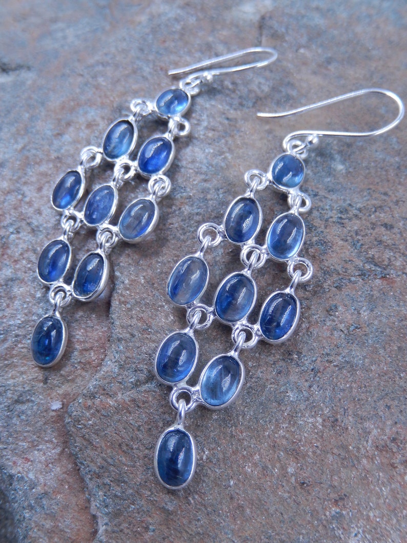 May include: Silver chandelier earrings with multiple tiers of oval, blue gemstones. The earrings have a cascading design, with each tier connected by silver links. The gemstones are a vibrant blue color, and the earrings have a hook closure.