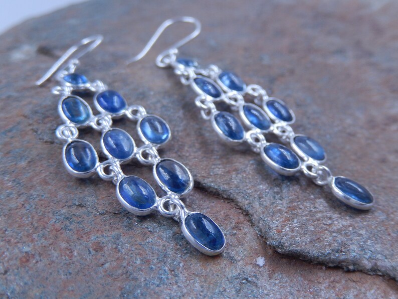May include: Elegant chandelier earrings with a cascade design. Each earring features multiple oval-shaped, deep blue gemstones set in a silver-toned metal. The gemstones are arranged in a tiered, flowing pattern, creating a sophisticated and eye-catching accessory.