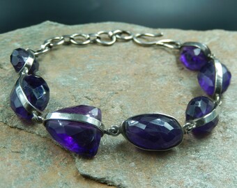 May include: A silver bracelet with a chain link design and multiple faceted amethyst stones. The stones are set in silver and have a deep purple colour.