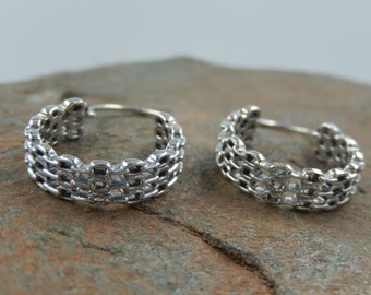 May include: Two silver hoop earrings with a woven design. The earrings are made of a series of interlocking circles.