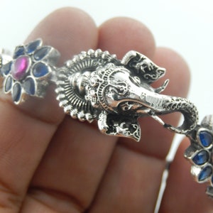 Könnte beinhalten: Silberarmband mit einem verzierten Elefantenkopf-Anhänger und blauen und rosa Blumenakzenten.