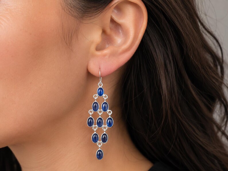 May include: Silver chandelier earrings with oval, deep blue gemstones. The earrings have a cascading design, with multiple gemstones arranged in a tiered pattern. The gemstones are set in a silver metal setting, and the earrings hang from a simple hook.