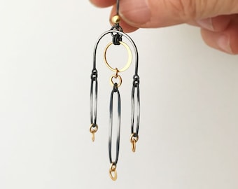 Könnte beinhalten: Schwarze und goldene Ohrringe mit einem Kreis und drei ovalen Formen, die an einem Bogen hängen.