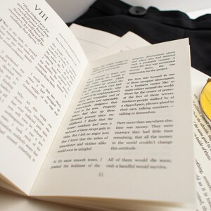 May include: Open book with printed text, pages fanned out. Yellow-tinted aviator sunglasses rest on the right side. A black garment is visible in the background.