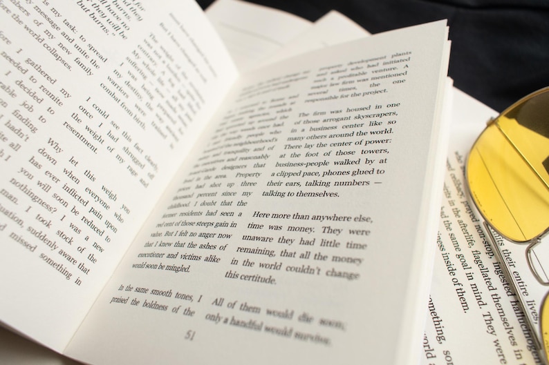 May include: An open book with printed text on cream-colored pages. Yellow-tinted sunglasses rest on the edge of the book. The book is slightly angled, with the text visible and in focus. The theme is literature.