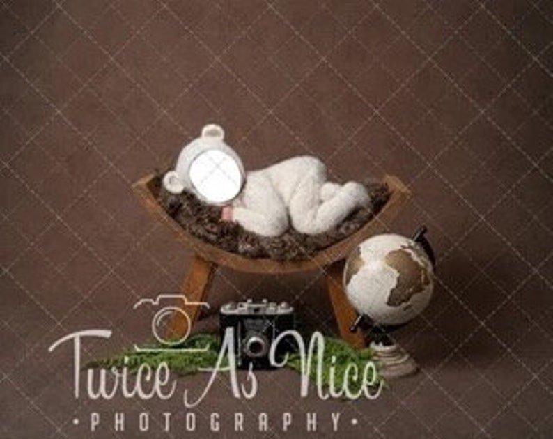 Puede incluir: Un disfraz de oso de peluche blanco en una cuna de madera marr&oacute;n con un globo terr&aacute;queo. La cuna est&aacute; sobre un soporte de madera con una c&aacute;mara vintage. El oso est&aacute; sobre una alfombra de piel marr&oacute;n.