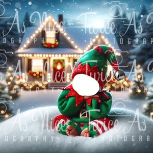 May include: A baby elf wearing a green and red elf costume sits in the snow in front of a house decorated for Christmas. The house has lights and a wreath on the door. There are snow-covered trees in the background.