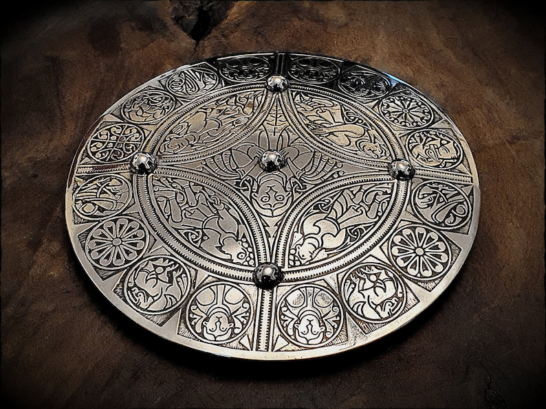 May include: A silver circular shield with intricate Celtic knotwork designs and four raised metal studs.