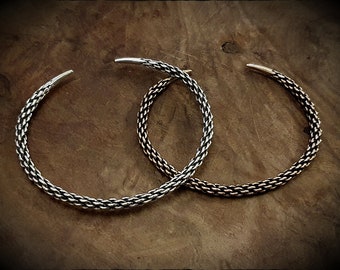 May include: Two silver bracelets with a braided design. The bracelets are on a wooden surface.