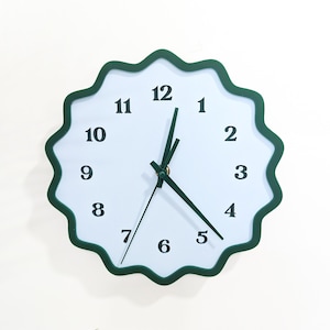 May include: A white wall clock with a dark green scalloped edge. The clock face is white with black numerals and dark green hands. The clock is round and has a simple, modern design.