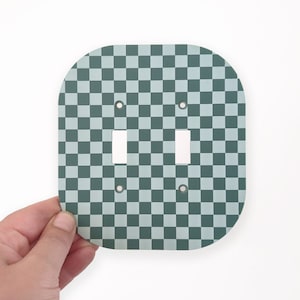 Puede incluir: Una placa de interruptor de luz cuadrada de cerámica con un diseño de cuadros verde claro y blanco y dos interruptores de palanca.