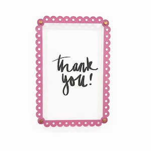 Puede incluir: Marco rosa con borde festoneado con las palabras "¡Gracias!" escritas en tinta negra.