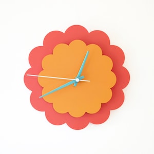 May include: A colourful wall clock with a red outer ring and an orange inner ring. The clock hands are teal blue and white.
