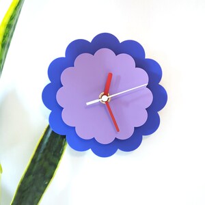 以下が含まれることがあります： 赤と白の針が付いた、紫と青の花の形をした壁掛け時計です。