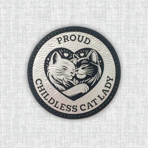 May include: A silver and black round patch with a heart-shaped design featuring two cats cuddling. The text "Proud Childless Cat Lady" is written around the heart.