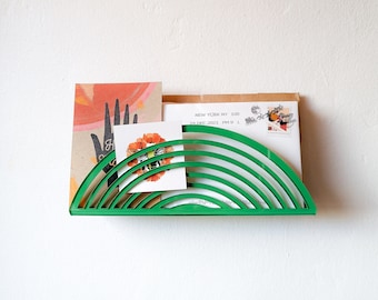 May include: Green rainbow-shaped mail holder with a card and envelope inside. The card has a bee and flower design and the envelope has the text "NEW YORK NY 100 24 DEC 2021 PM 9 L."
