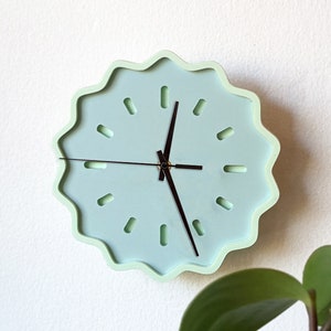 May include: A light blue wall clock with a wavy, scalloped edge. The clock has black hands and a simple design with no numbers.