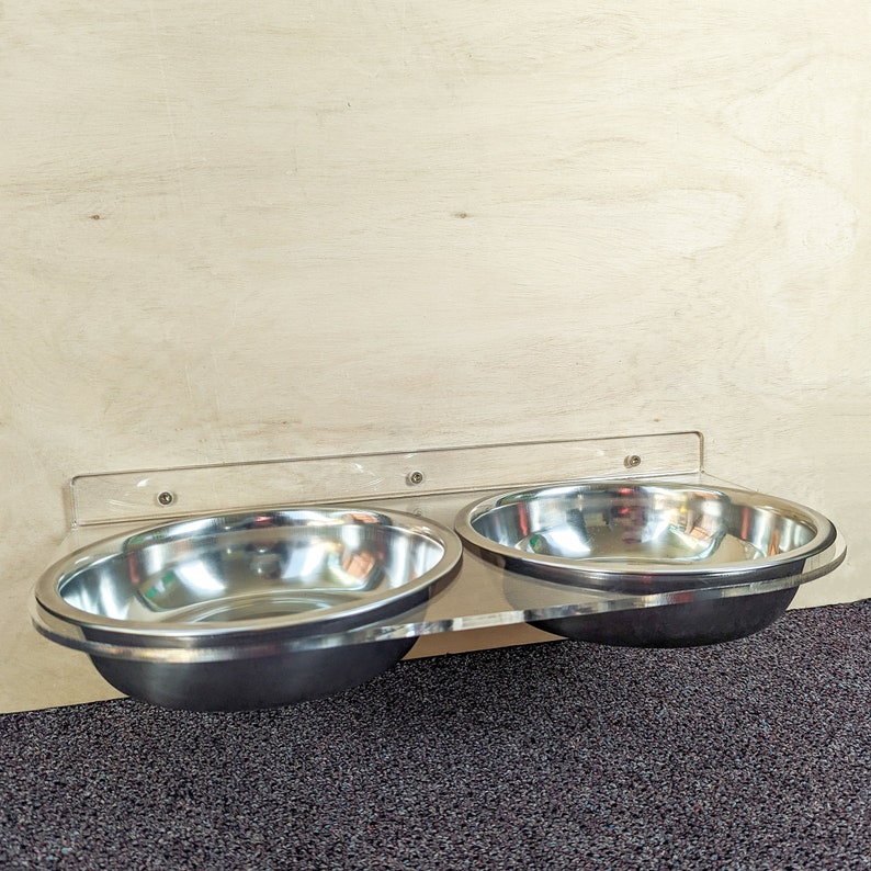 Pu&ograve; includere: Due ciotole in acciaio inox per animali domestici montate su un supporto a parete in acrilico trasparente. Le ciotole sono vuote e pronte per il cibo o l'acqua.